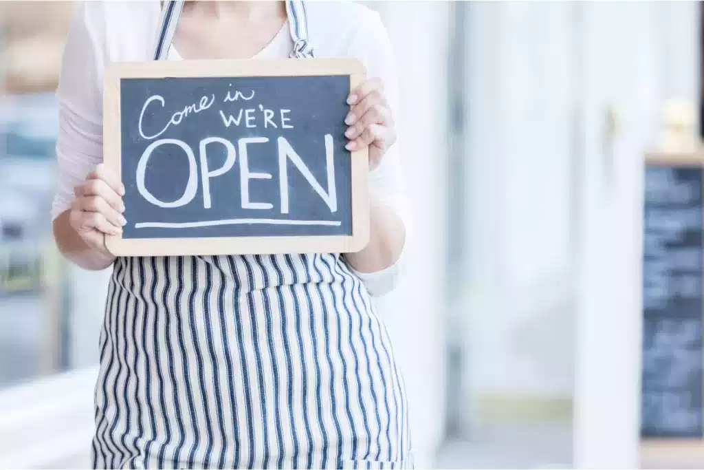 Someone holding a sign that says "Come in we're open."