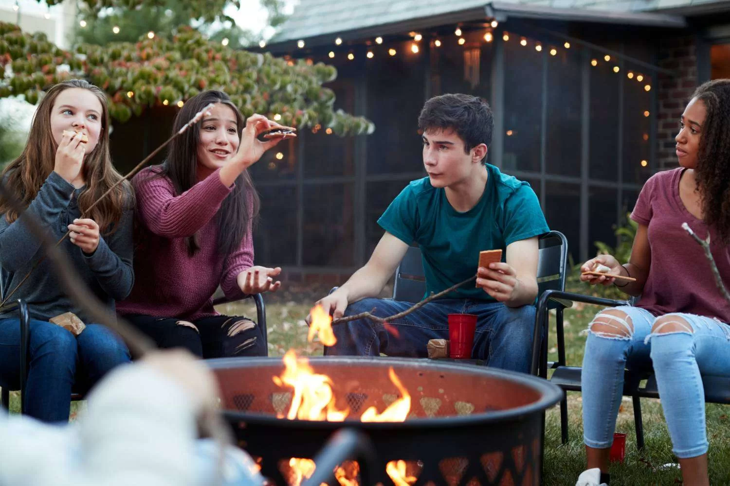 Teens around a campfire enjoying snores.