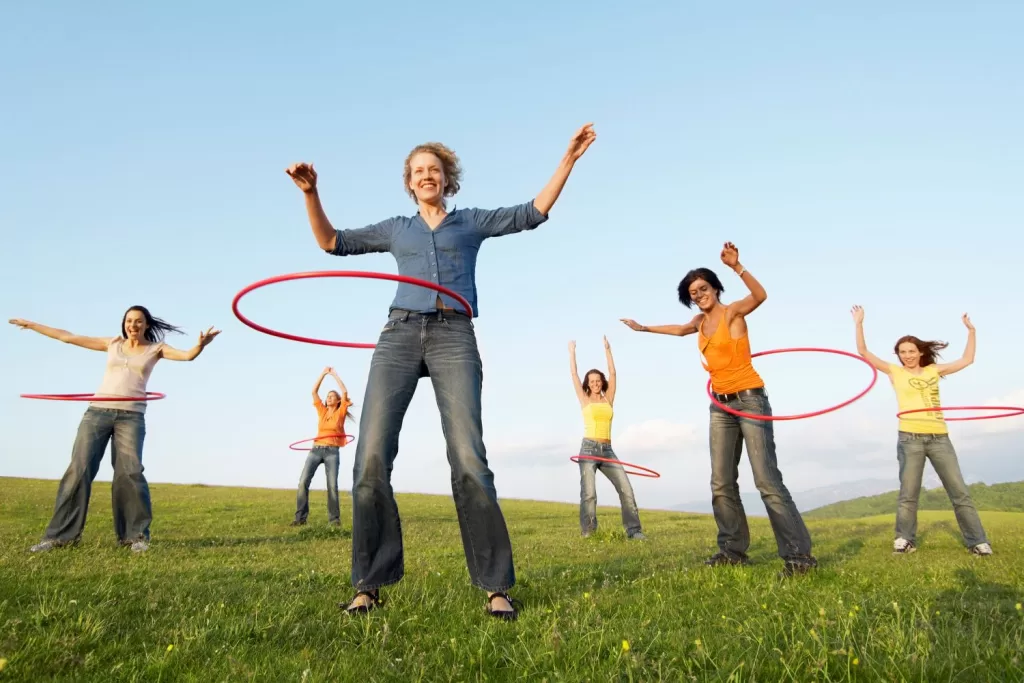 Several woman enjoying movement in the park by hula hooping.