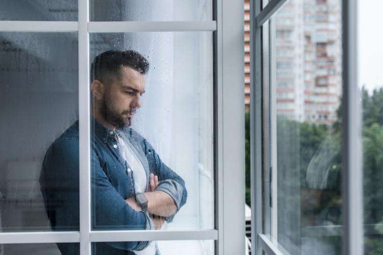 Man struggling with social isolation and eating disorder looking out the window.