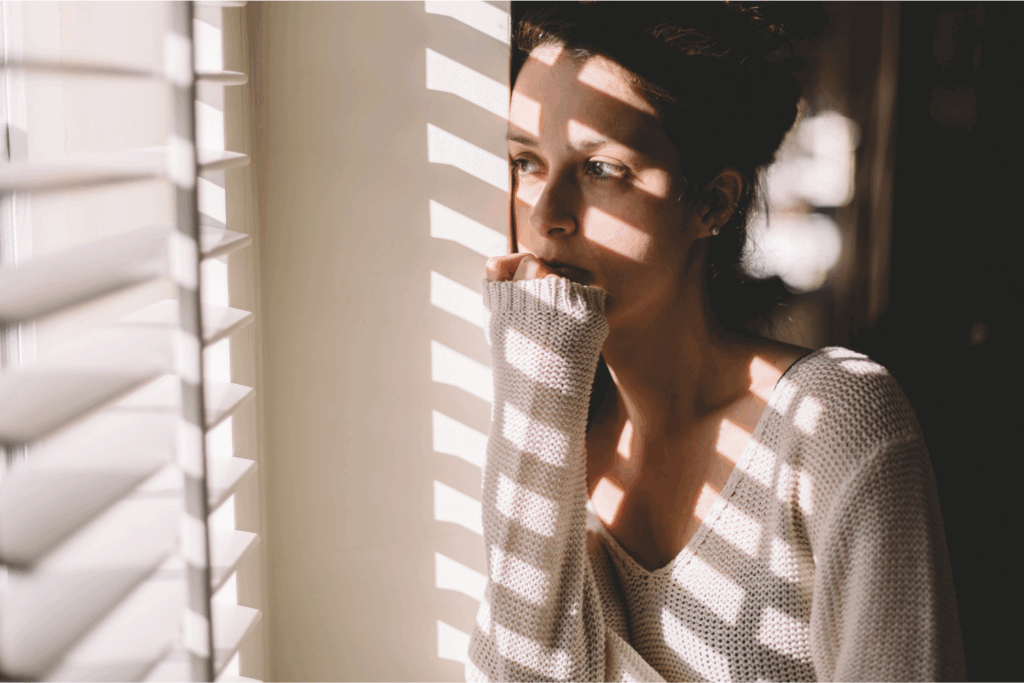 A woman looking out the window in winter, reflecting on emotions and shorter days and eating disorders